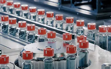 Herstellung von Arzneimitteln: Mehrere Glasfläschchen mit roten Deckeln stehen in einer Produktionsanlage.