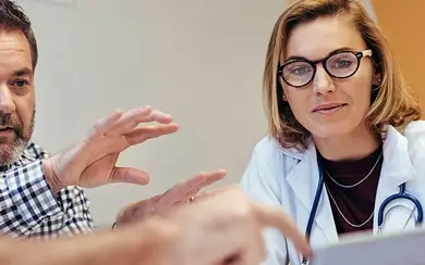 Mehrere Personen aus verschiedenen Gesundheitsberufen, darunter eine Ärztin mit Stethoskop, sitzen gemeinsam an einem Tisch und besprechen sich.