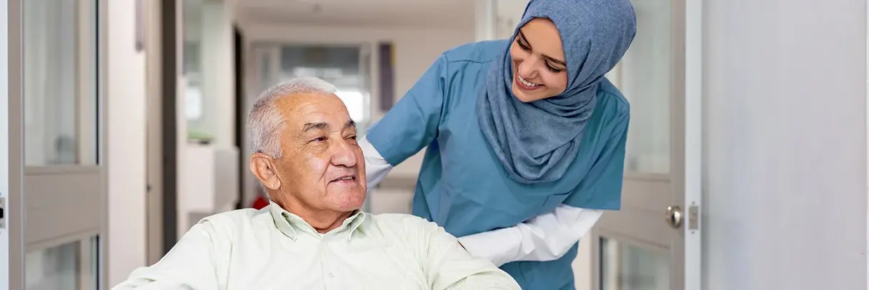 Pflegekraft mit einem älteren Mann Pflegekraft mit Kopftuch im Gespräch mit einem älteren Mann in einer Pflegeeinrichtung.