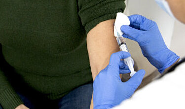 Arzt mit Schutzkleidung impft eine Patientin (Symbolbild)
