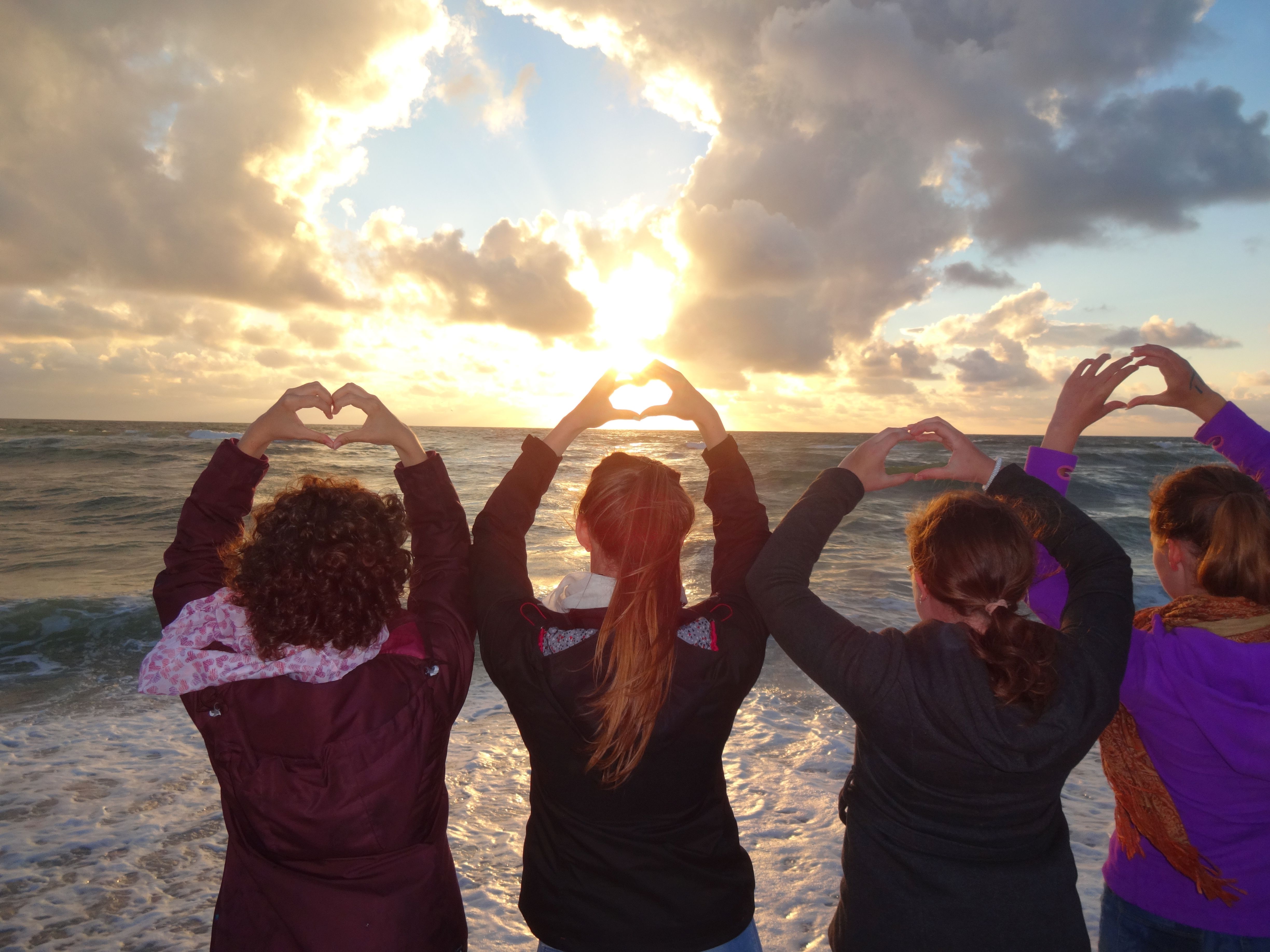Vier Teilnehmerinnen von Meeresrauschen stehen am Strand und formen Herzen mit ihren Händen.