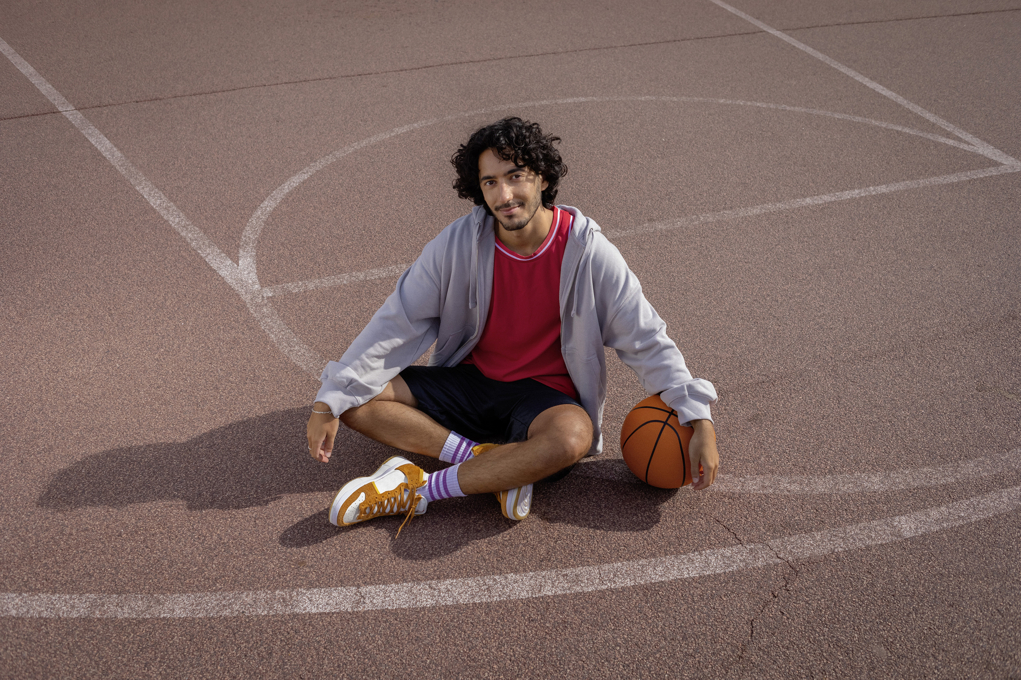 Ein Student sitzt im Schneidersitz auf einem Basketballplatz.