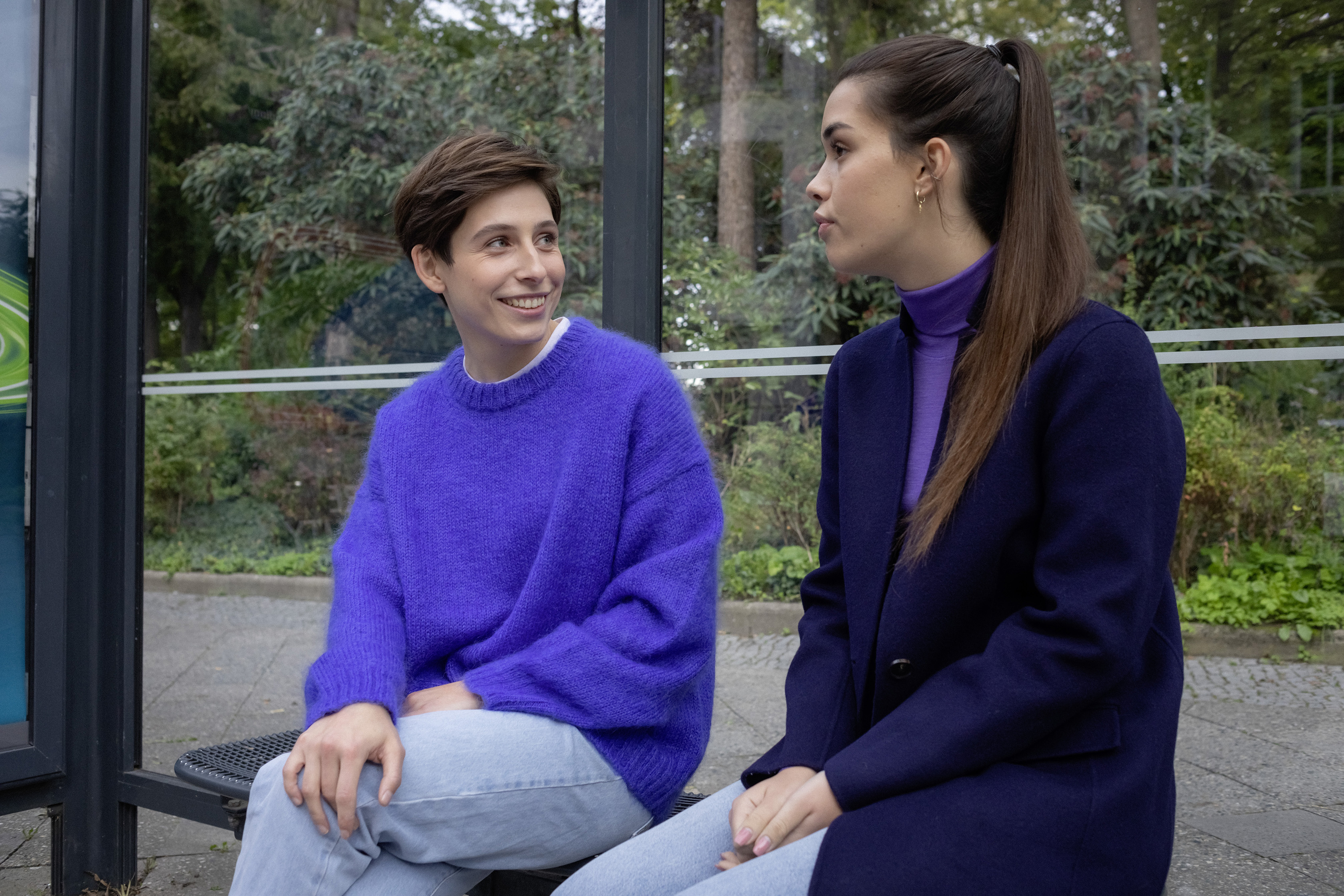 Zwei Studentinnen unterhalten sich an einer Bushaltestelle.