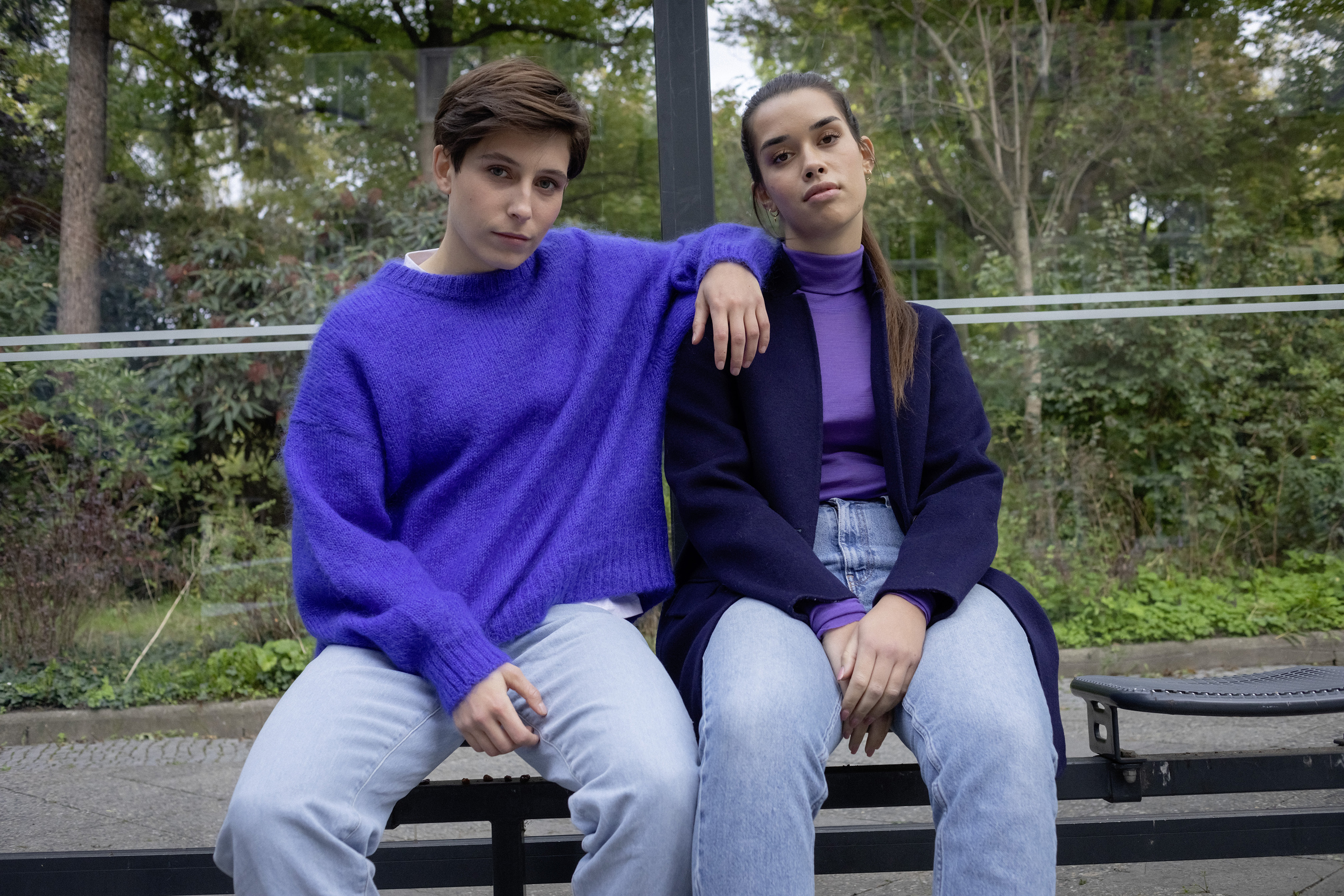 Zwei junge Frauen sitzen an einer Bushaltestelle