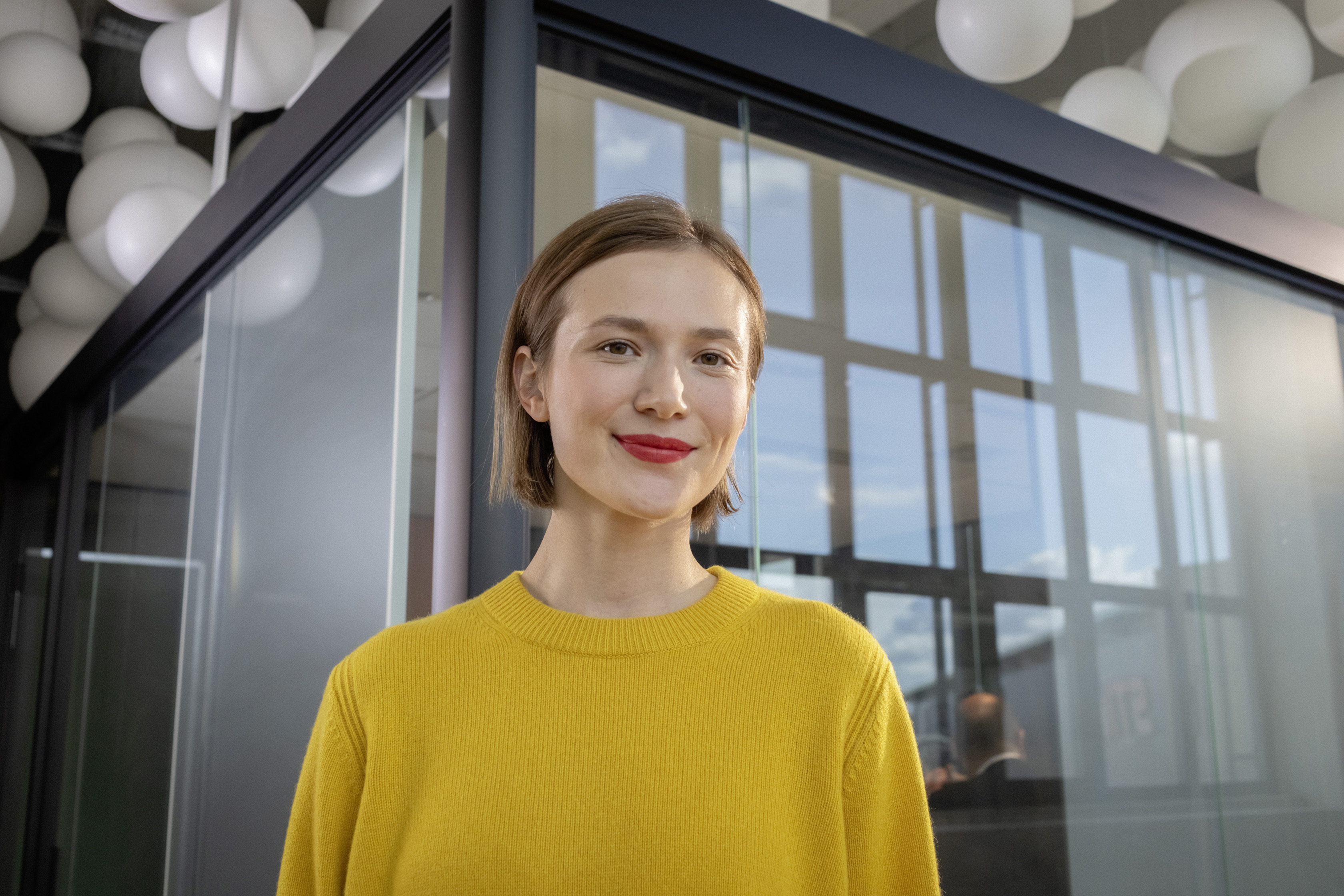 Eine junge Berufserfahrene steht mit vor einem verglasten Raum.