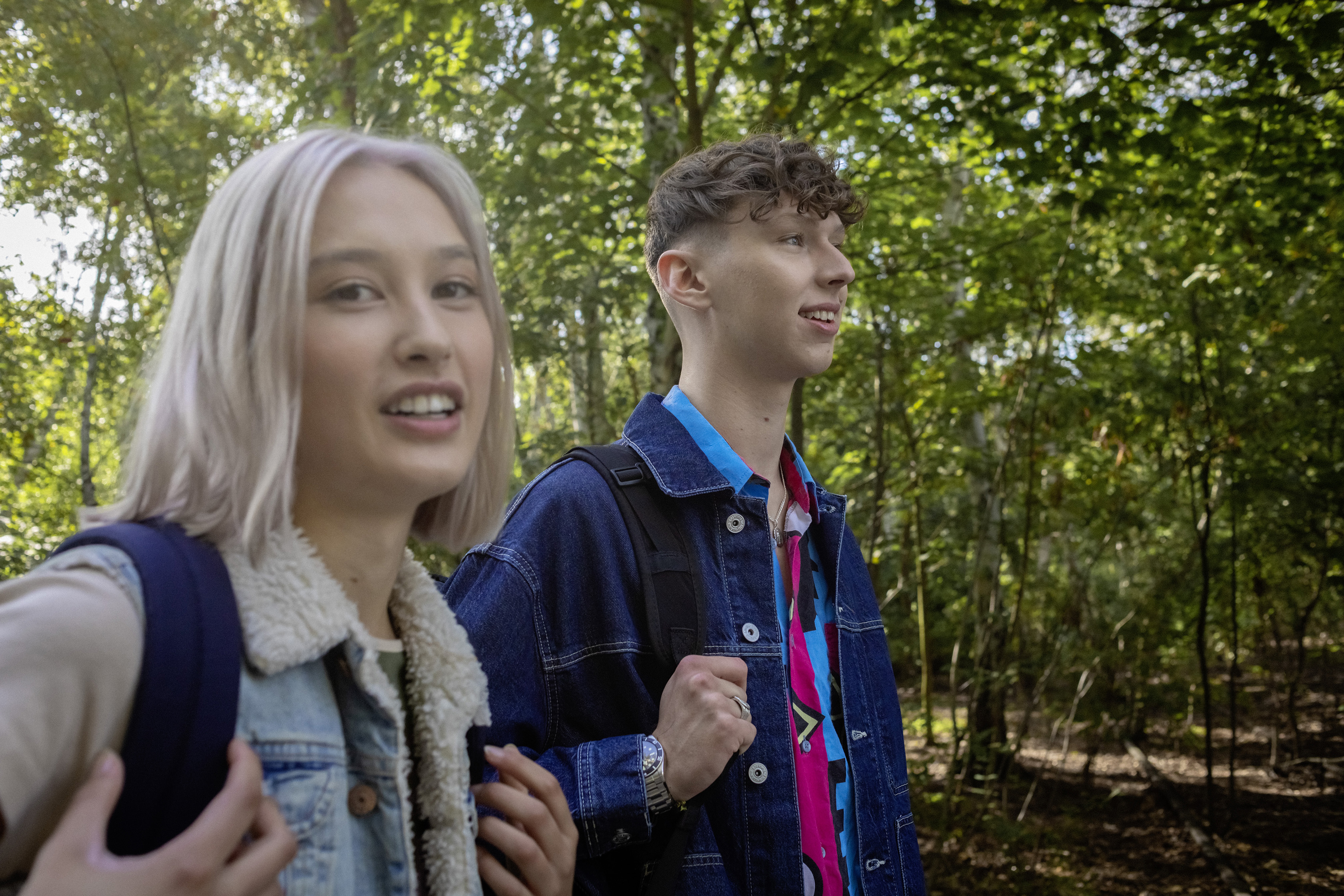 Eine Schülerin und ein Schüler laufen mit Rucksäcken durch den Park.