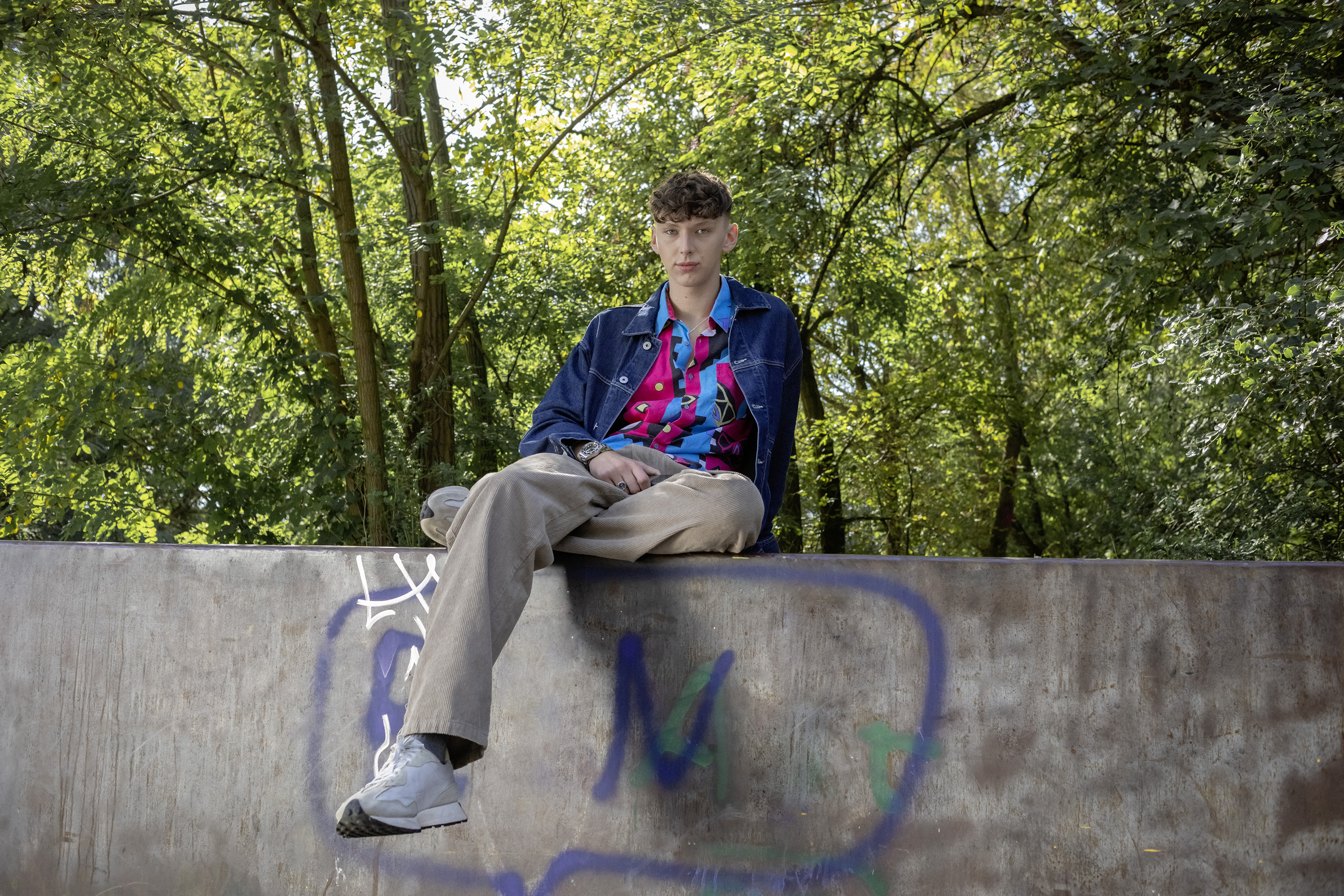 Ein Schüler sitzt auf einer Mauer im Park.