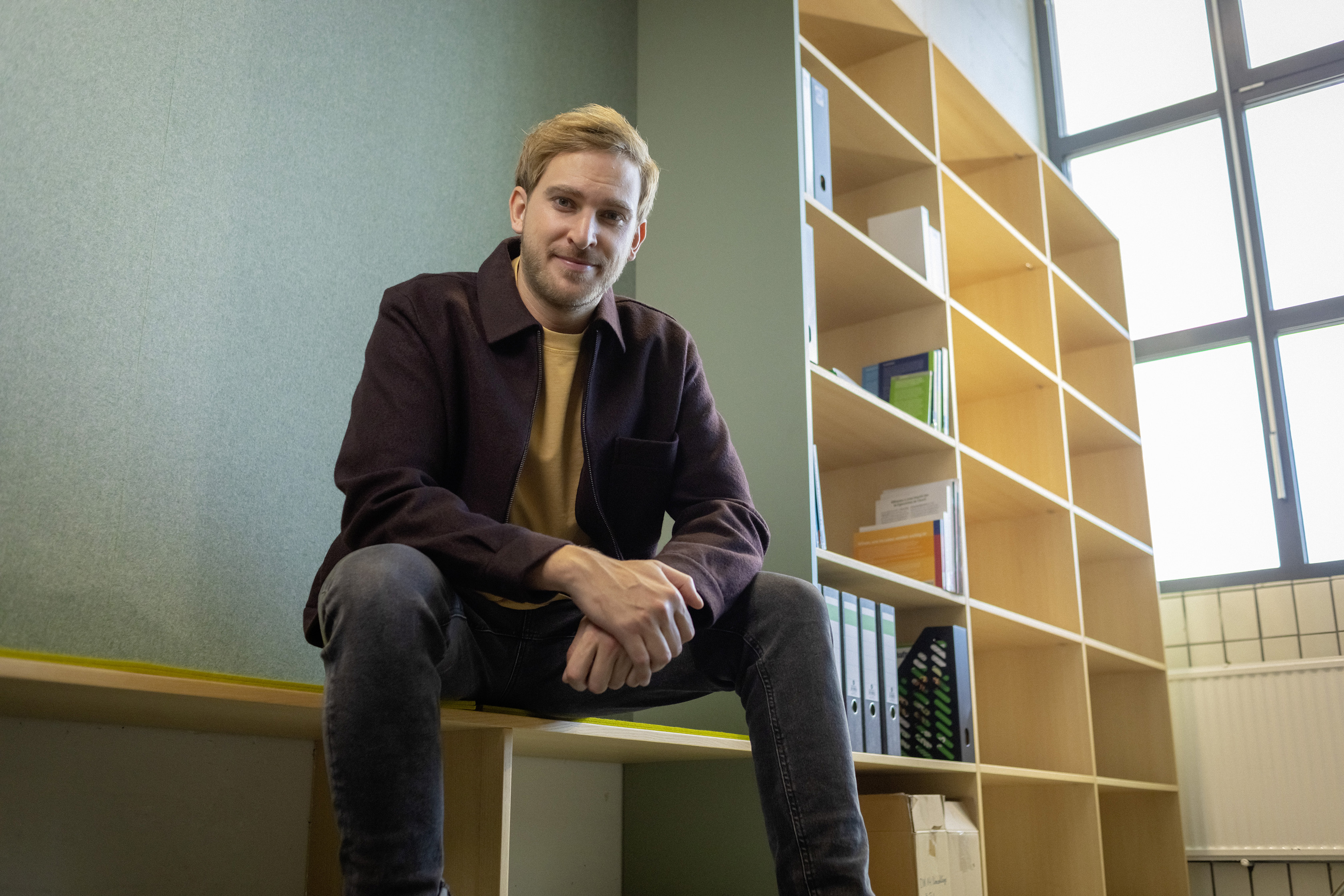 Ein junger Berufserfahrener sitzt vor einem Bücherregal.