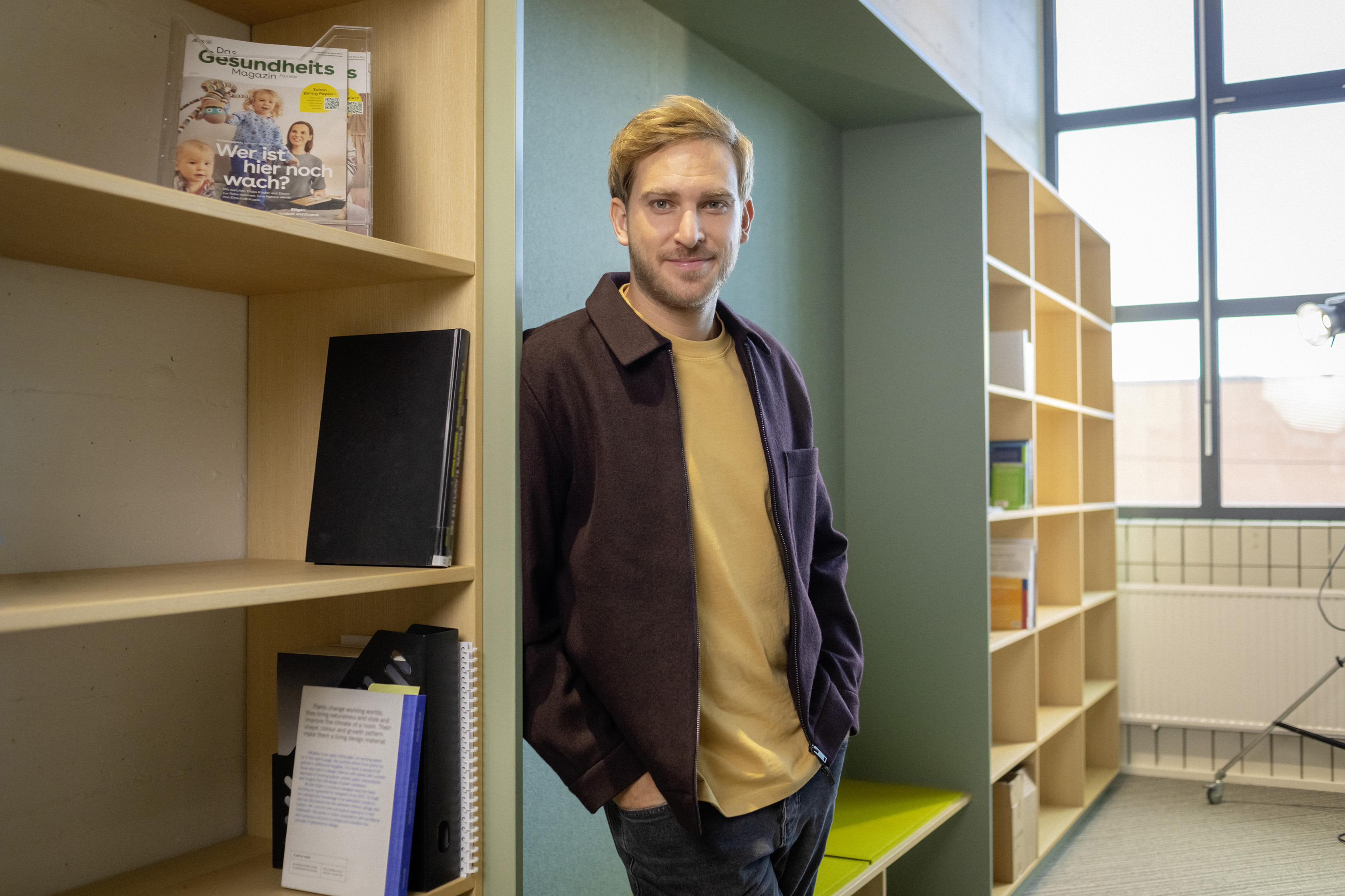 Ein junger Berufserfahrener lehnt an einem Bücherregal.