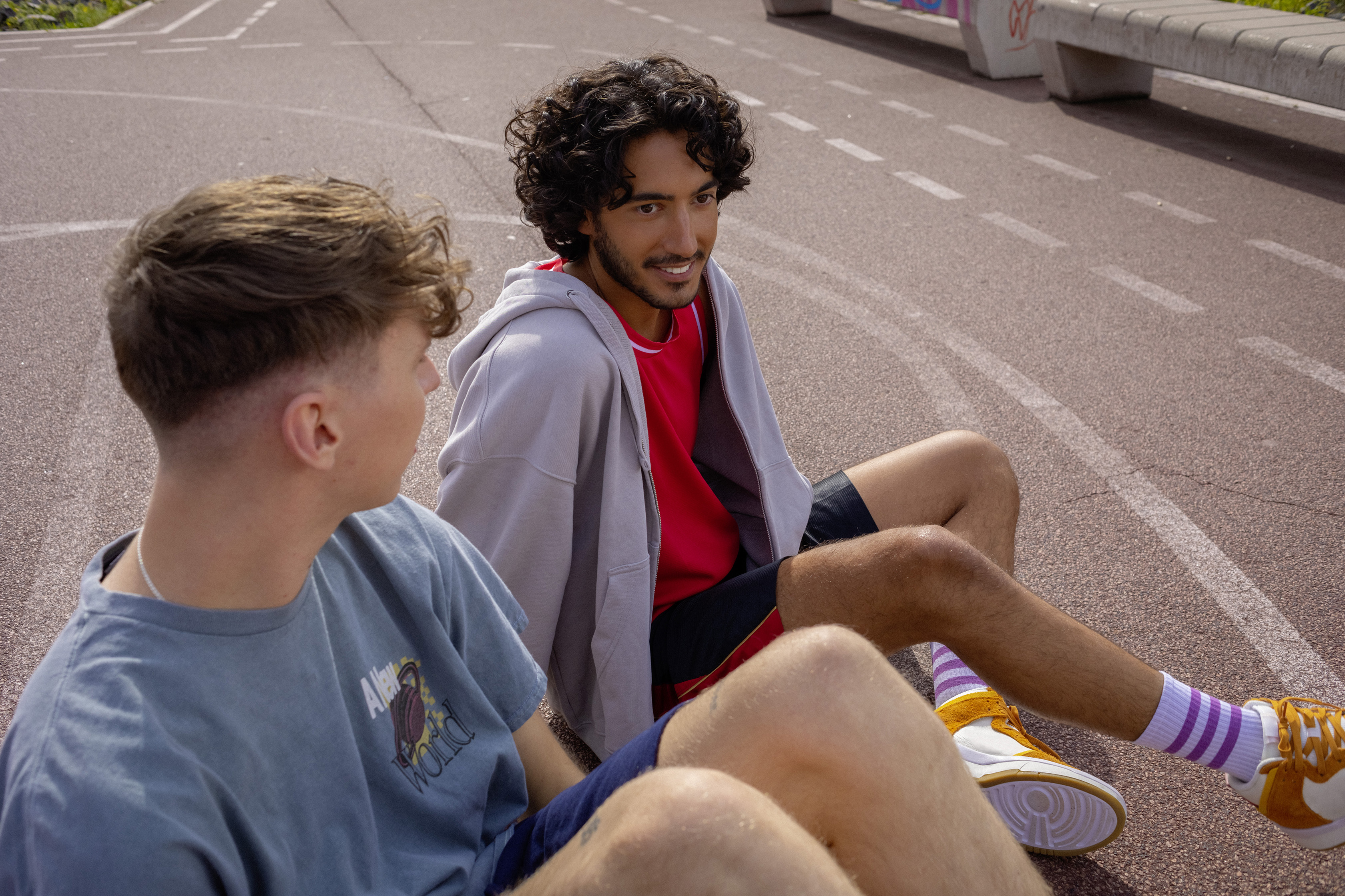 Ein Student und ein Schüler sitzen auf einem Basketballplatz und unterhalten sich.
