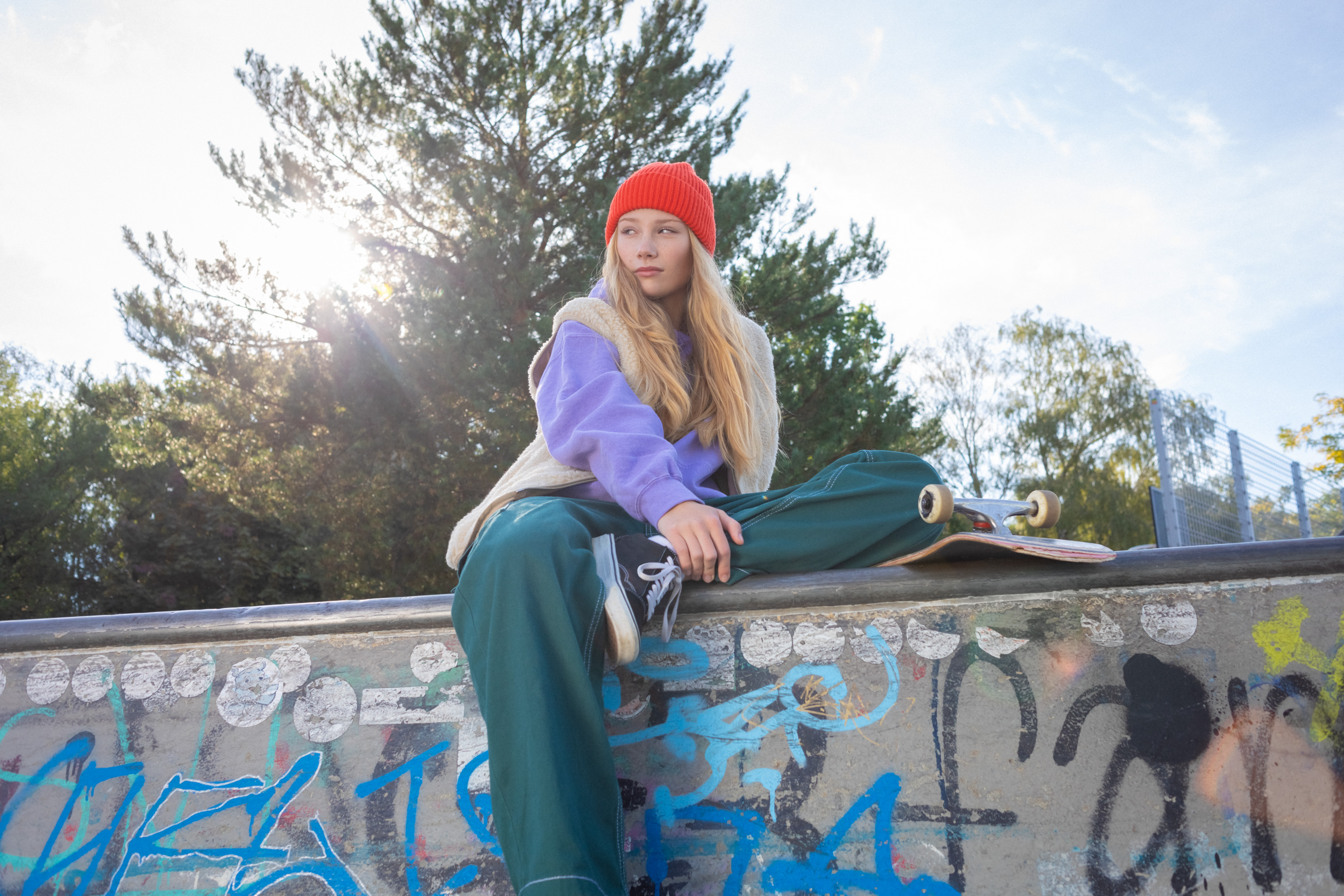 Eine Schülerin sitzt mit Skateboard auf einer Mauer.
