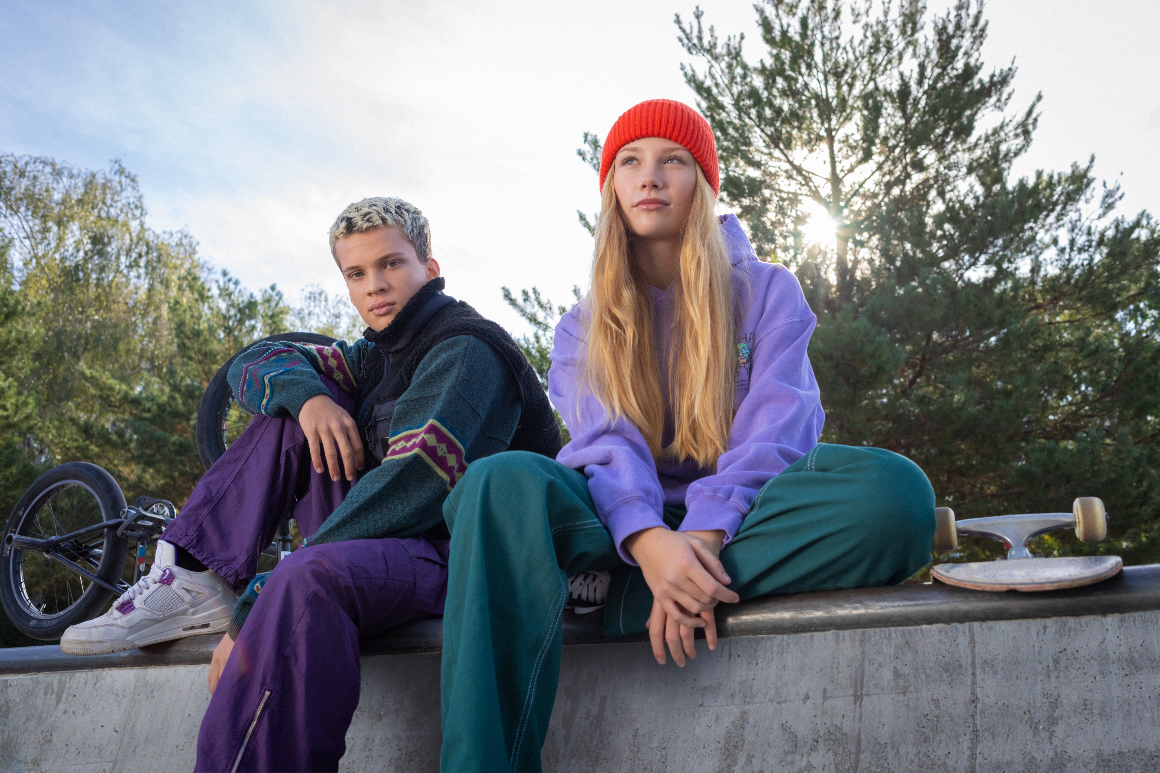 Eine Schülerin mit Skateboard und ein Schüler sitzen auf einer Mauer.