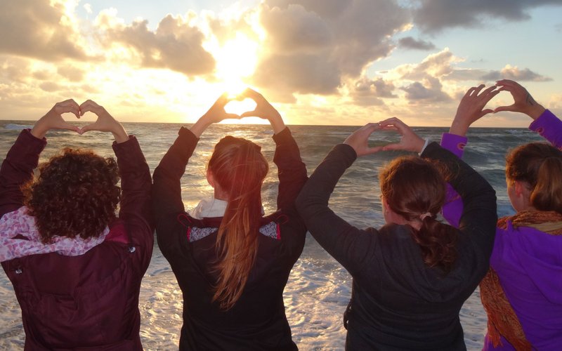 Vier Teilnehmerinnen von Meeresrauschen stehen am Strand und formen Herzen mit ihren Händen.