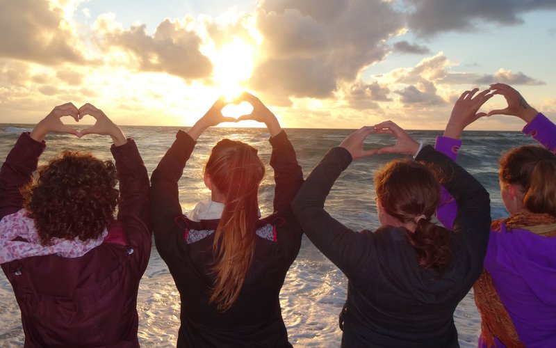Vier Teilnehmerinnen von Meeresrauschen stehen am Strand und formen Herzen mit ihren Händen.