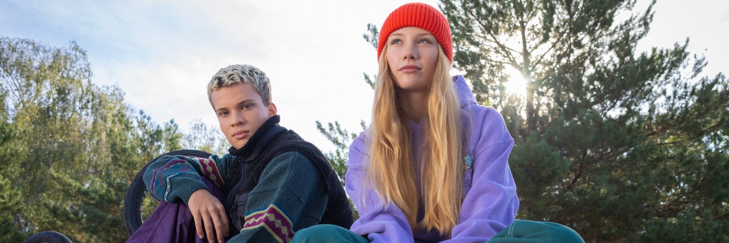 Eine Schülerin mit Skateboard und ein Schüler sitzen auf einer Mauer.