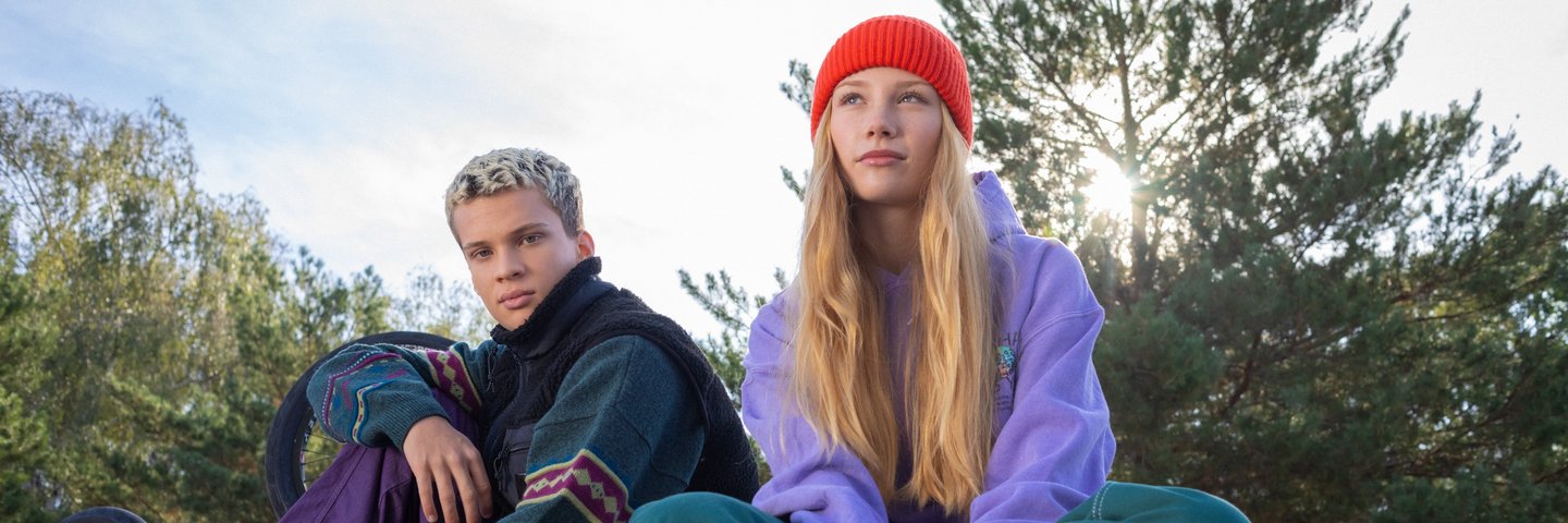Eine Schülerin mit Skateboard und ein Schüler sitzen auf einer Mauer.