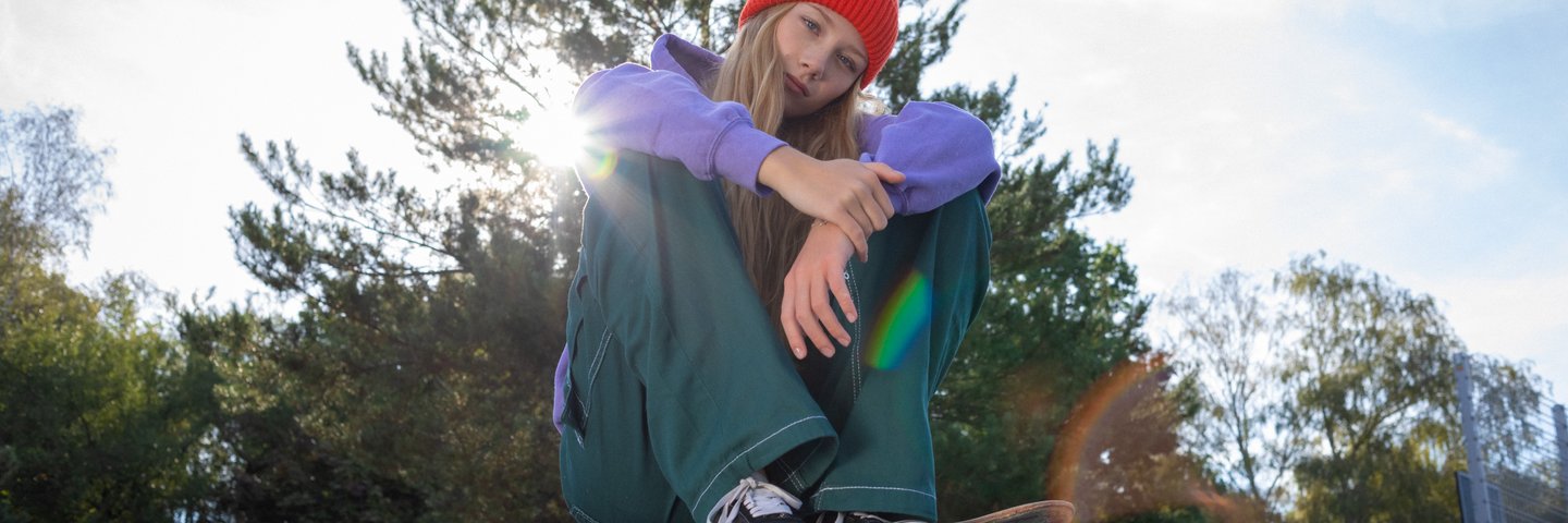 Eine Schülerin sitzt mit Skateboard im Skatepark.