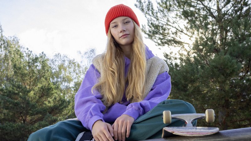 Eine Schülerin sitzt mit ihrem Skateboard auf einer Mauer.