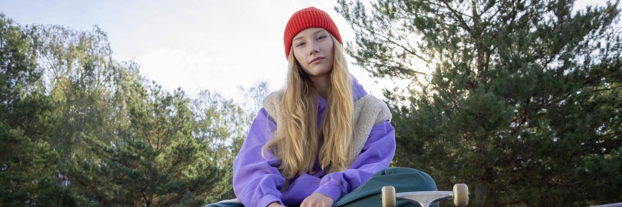 Eine Schülerin sitzt mit ihrem Skateboard auf einer Mauer.