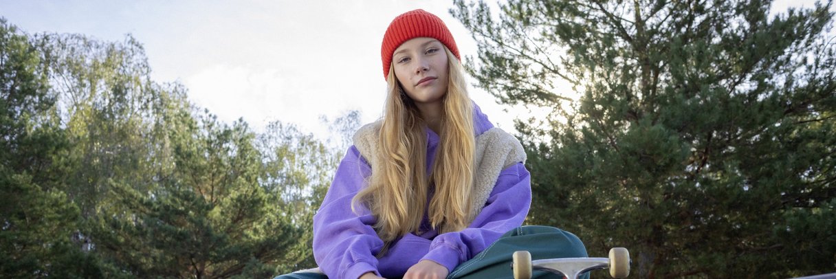 Eine Schülerin sitzt mit ihrem Skateboard auf einer Mauer.