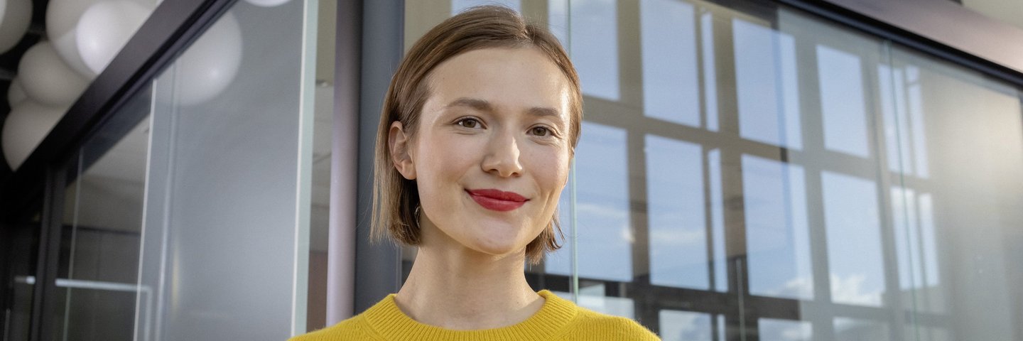 Eine junge Berufserfahrene steht mit vor einem verglasten Raum.