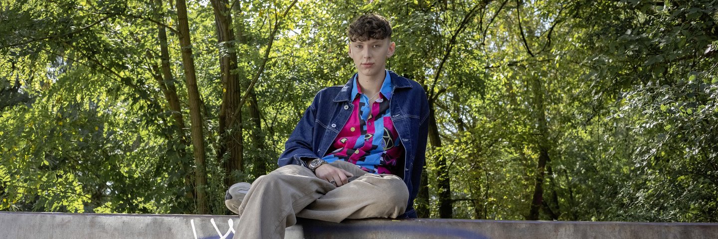 Ein Schüler sitzt auf einer Mauer im Park.