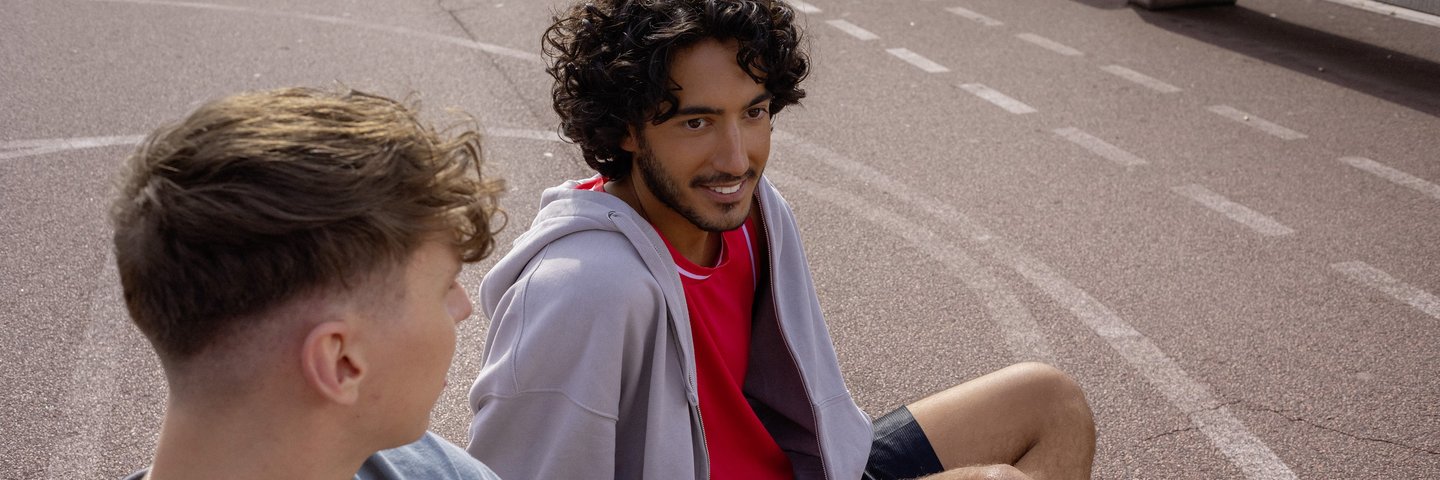 Ein Student und ein Schüler sitzen auf einem Basketballplatz und unterhalten sich.