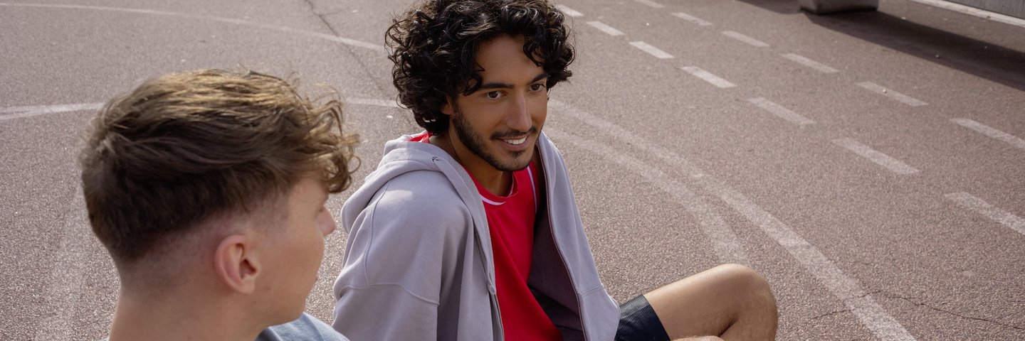 Ein Student und ein Schüler sitzen auf einem Basketballplatz und unterhalten sich.