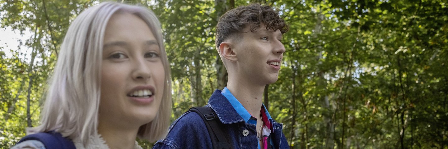 Eine Schülerin und ein Schüler laufen mit Rucksäcken durch den Park.