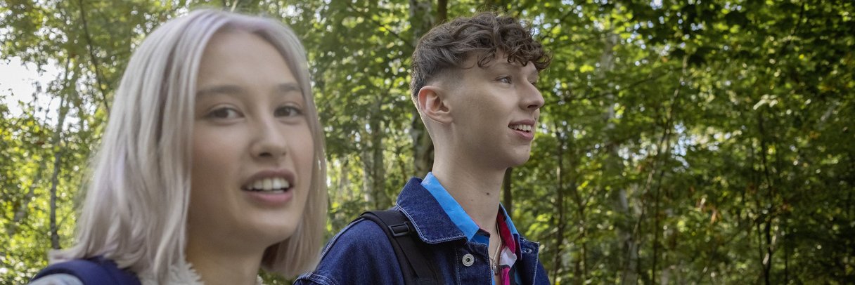 Eine Schülerin und ein Schüler laufen mit Rucksäcken durch den Park.