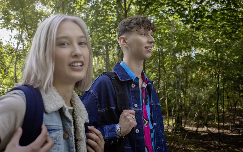 Eine Schülerin und ein Schüler laufen mit Rucksäcken durch den Park.
