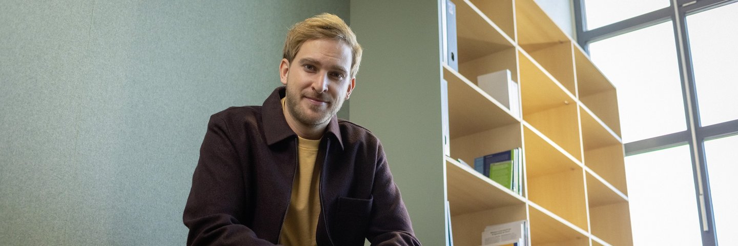 Ein junger Berufserfahrener sitzt vor einem Bücherregal.