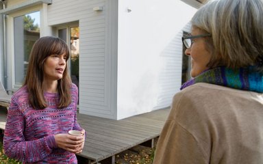 Zwei Frauen unterhalten sich im Garten eines Hauses.