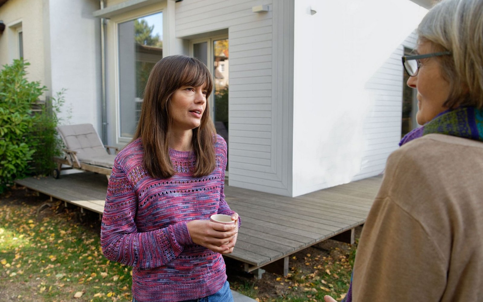 Zwei Frauen unterhalten sich im Garten eines Hauses.