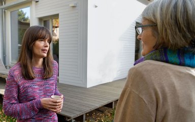 Zwei Frauen unterhalten sich im Garten eines Hauses.