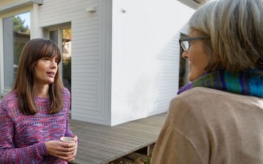 Zwei Frauen unterhalten sich im Garten eines Hauses.