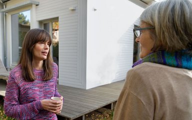 Zwei Frauen unterhalten sich im Garten eines Hauses.