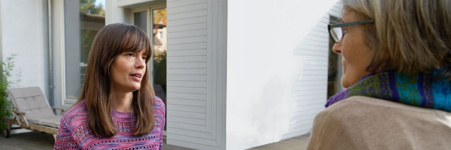 Zwei Frauen unterhalten sich im Garten eines Hauses.