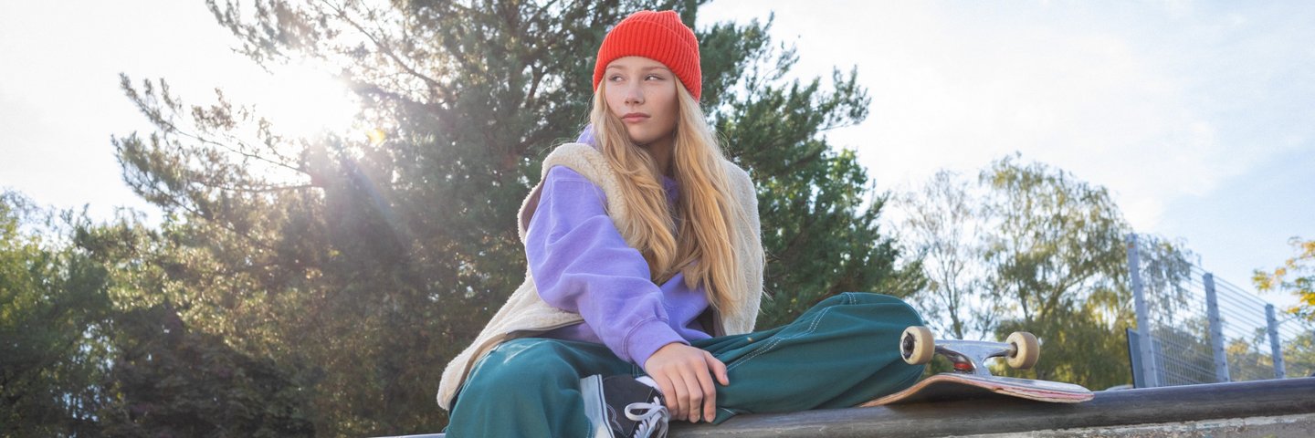 Eine Schülerin sitzt mit Skateboard auf einer Mauer.