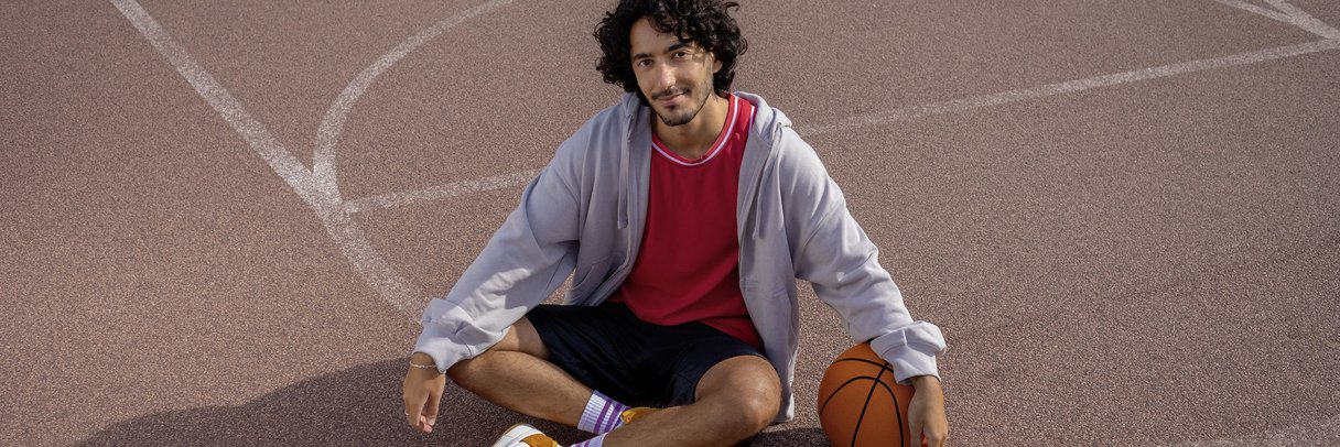 Ein Student sitzt im Schneidersitz auf einem Basketballplatz.