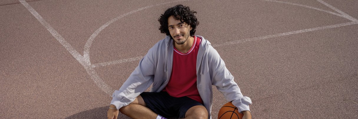Ein Student sitzt im Schneidersitz auf einem Basketballplatz.