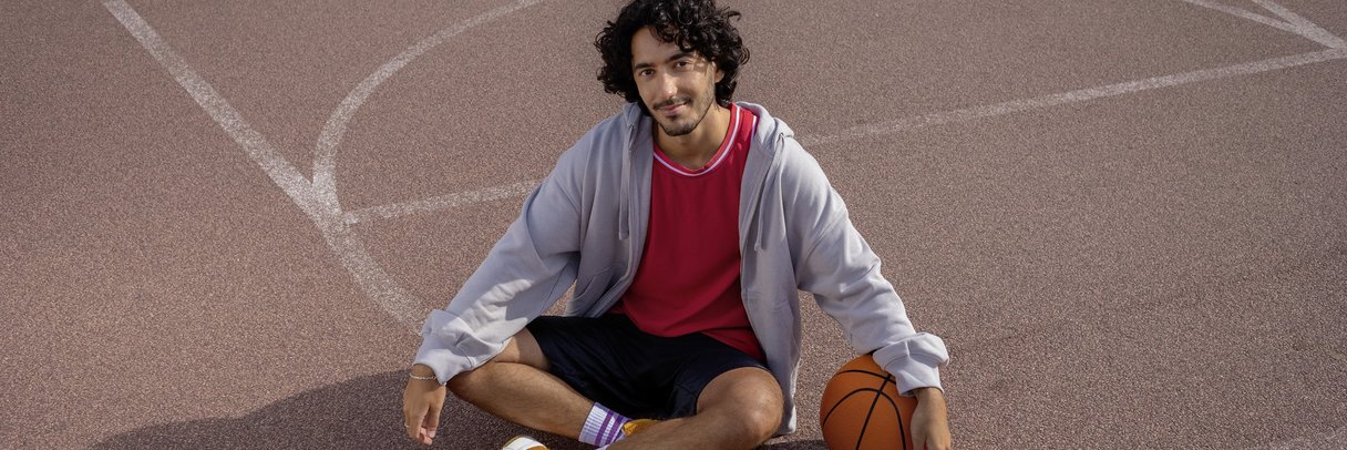 Ein Student sitzt im Schneidersitz auf einem Basketballplatz.