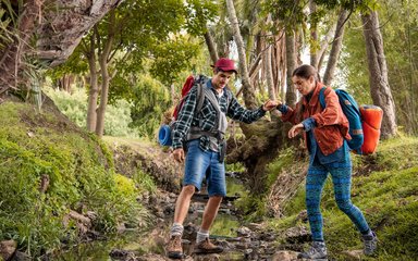 Ein Wanderführer hilft einer Wanderin über einen Bachlauf.
