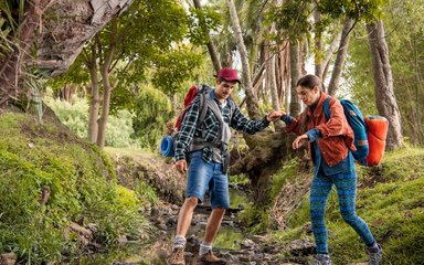 Ein Wanderführer hilft einer Wanderin über einen Bachlauf.