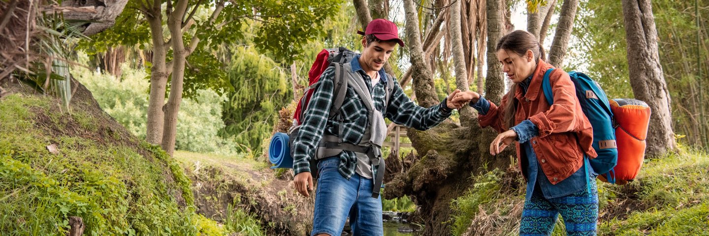 Ein Wanderführer hilft einer Wanderin über einen Bachlauf.