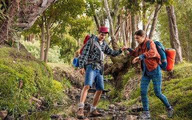 Ein Wanderführer hilft einer Wanderin über einen Bachlauf.