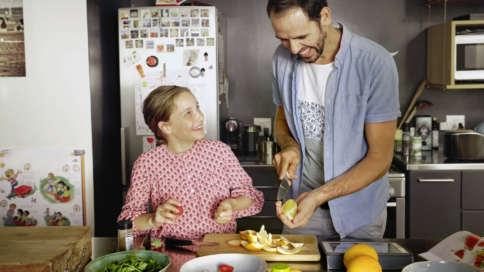 Erwachsene Person und Kind bereiten gemeinsam Obst in der Küche zu und lachen sich dabei an.