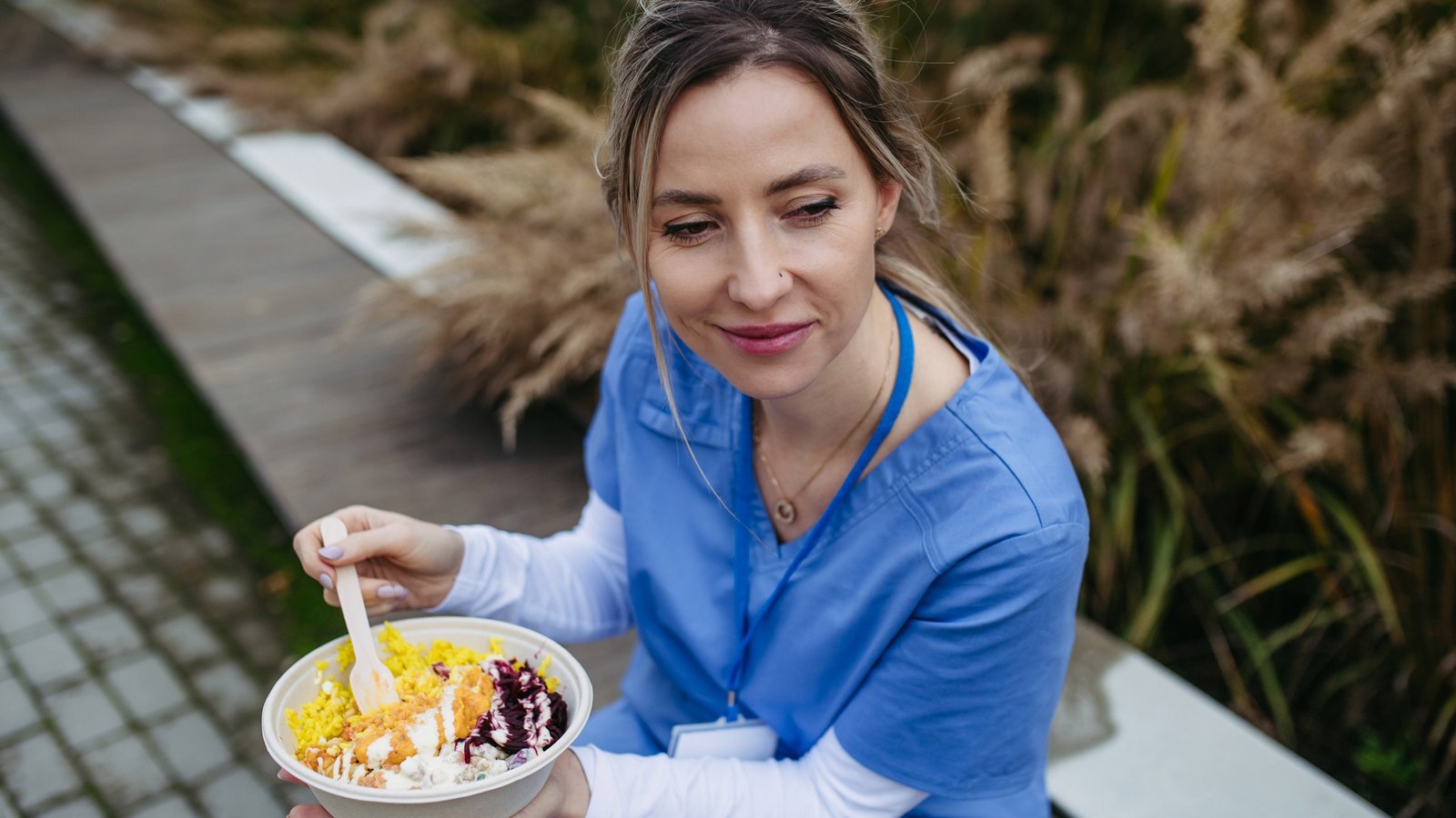 Eine junge Pflegekraft sitzt draußen auf einer Bank und isst.