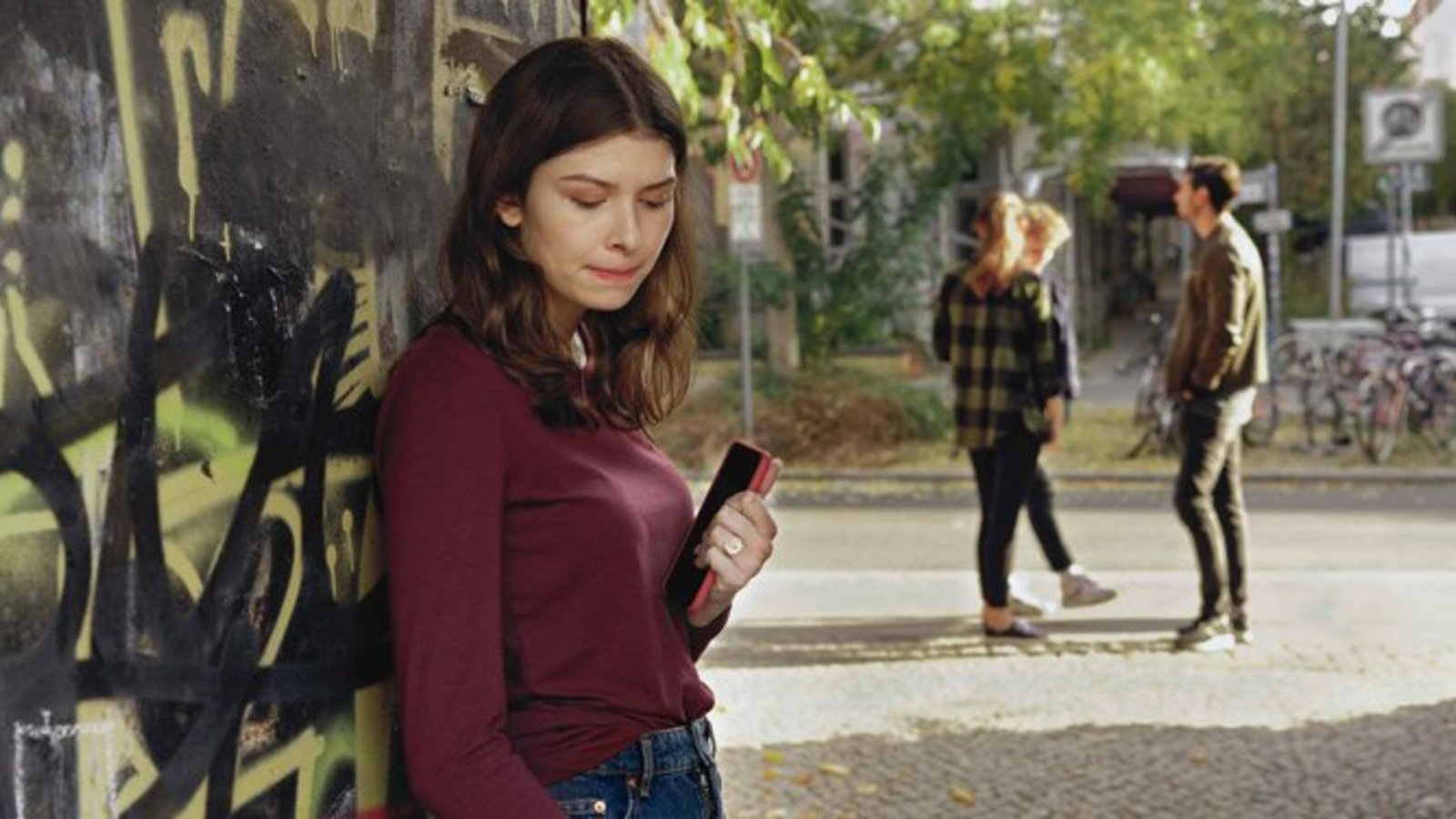 Mädchen versteckt sich mit Handy in der Hand vor anderen Jugendlichen.