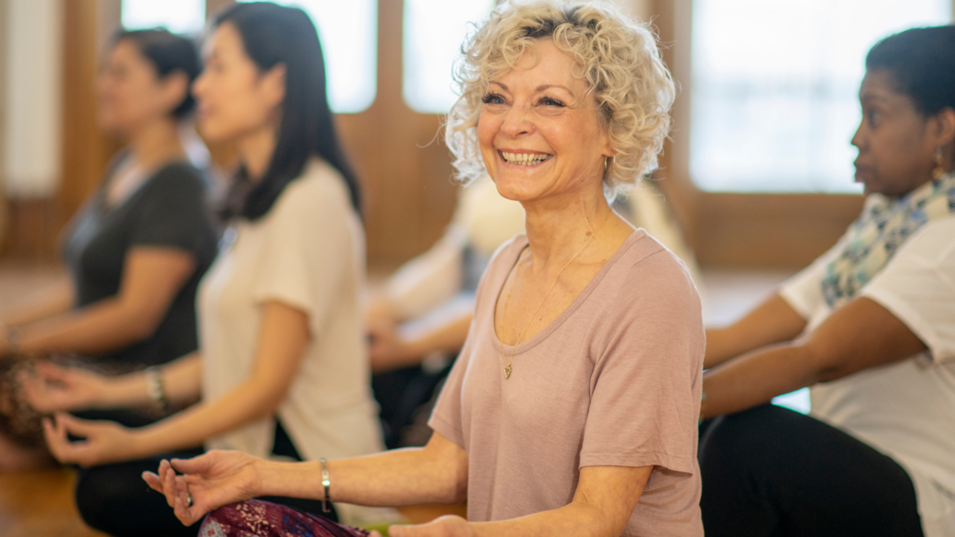Eine lachende Frau sitzt in einer Gruppe von Frauen, die Yoga machen.